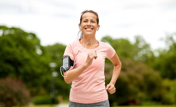 イヤホン付きの女性は公園で腕章ジョギングを追加します — ストック写真