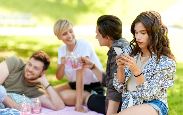 Kvinna med smartphone på picknick med vänner — Stockfoto