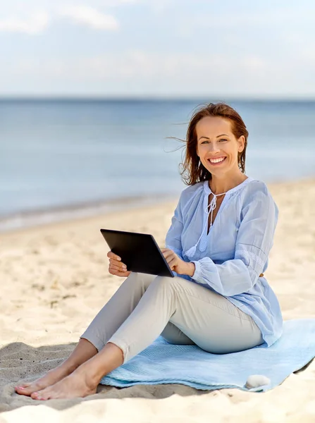 Felice donna sorridente con tablet pc sulla spiaggia estiva Foto Stock