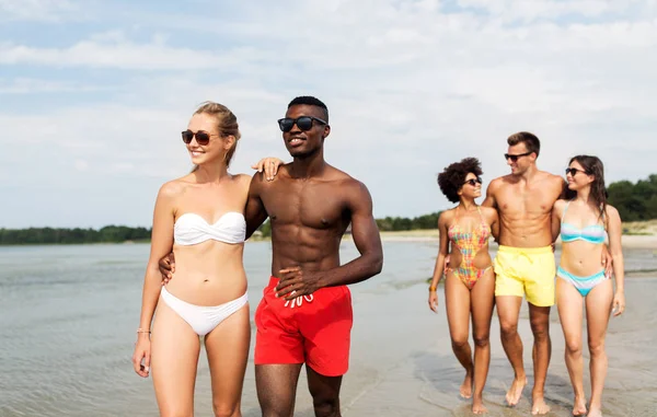 Gemengd ras paar wandelen langs het strand met vrienden — Stockfoto