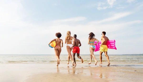 Freunde laufen mit Beachball und Badematratze — Stockfoto