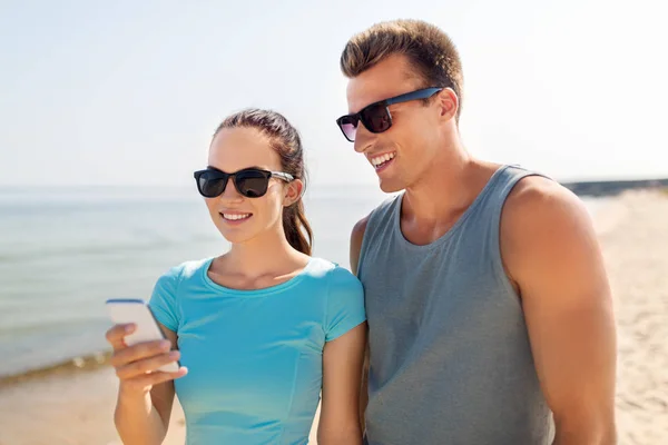 Couple in sports clothes with smartphones on beach — Stock Photo, Image