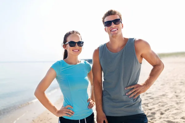 Feliz pareja en ropa deportiva y sombras en la playa — Foto de Stock