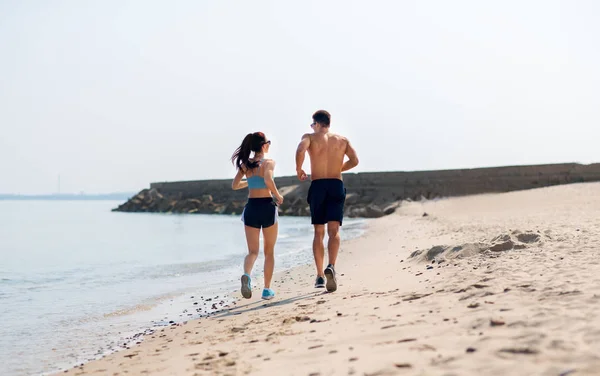 Casal em roupas esportivas correndo ao longo da praia — Fotografia de Stock