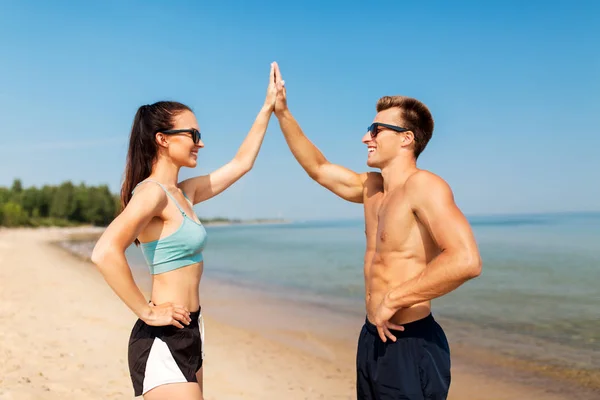 Casal feliz em roupas esportivas e tons na praia — Fotografia de Stock
