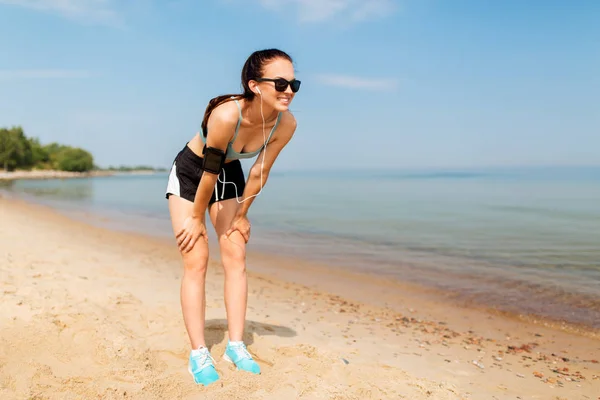 Corredor femenino con auriculares y brazalete en la playa — Foto de Stock