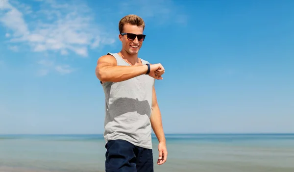 Счастливый мужчина с фитнес-трекером на летнем пляже — стоковое фото
