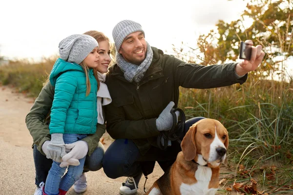 Счастливая семья с собакой, делающей селфи осенью — стоковое фото