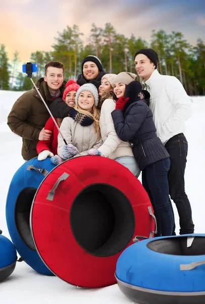レジャー 技術と人のコンセプト グループ雪代友達に笑顔のチューブ写真撮影スマート フォン Selfie スティック屋外で冬の自然な背景の上 — ストック写真
