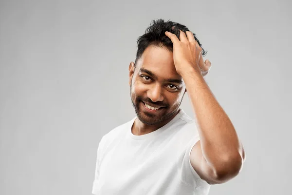 Indischer Mann berührt seine Haare vor grauem Hintergrund — Stockfoto
