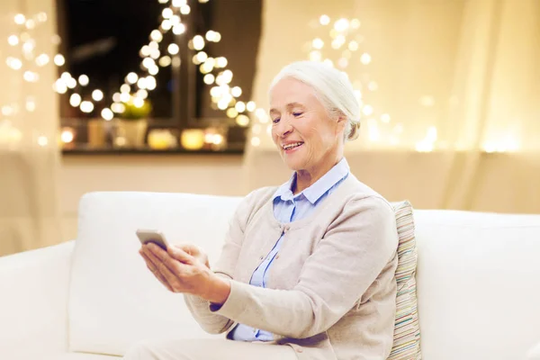 Пожилая женщина со смартфоном дома на Рождество — стоковое фото