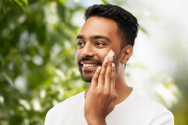 Hombre aplicando crema a cara sobre fondo natural —  Fotos de Stock