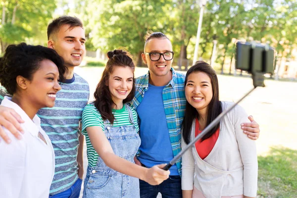 Amigos felices tomando fotos con selfie stick en el parque — Foto de Stock