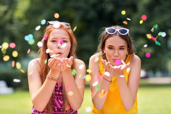 Teenage girls blowing confetti off hands in park — Stock Photo, Image