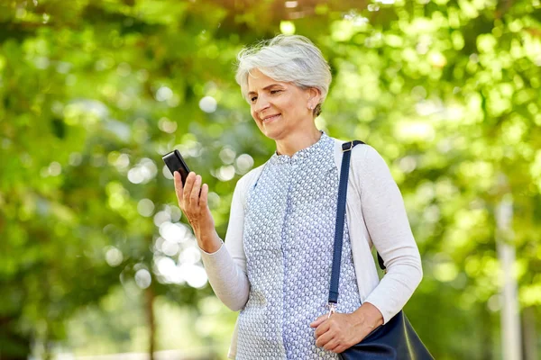 夏の公園でスマート フォンを持つ幸せな年配の女性 — ストック写真