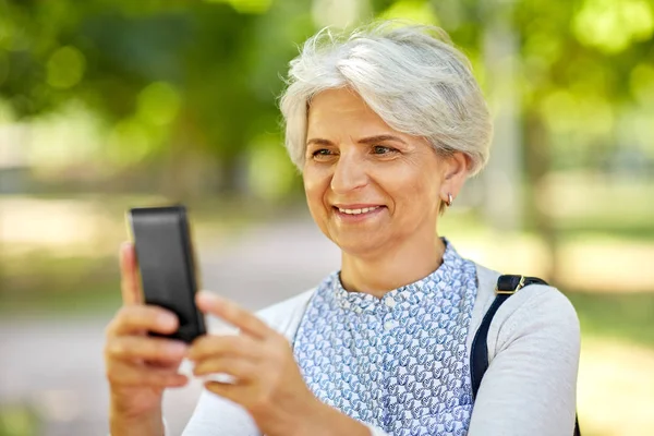 Senior vrouw fotograferen door cel in zomer park — Stockfoto