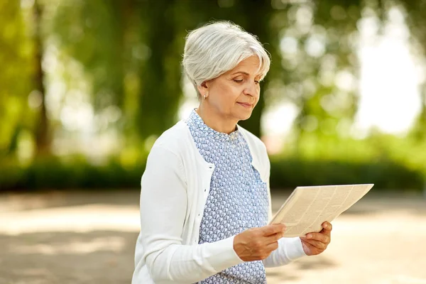 Старша жінка читає газету в літньому парку — стокове фото