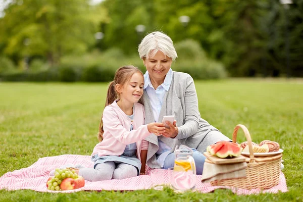 Mormor och barnbarn med cell på park — Stockfoto