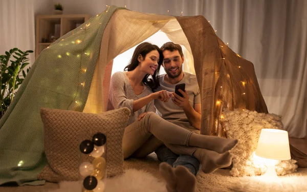 Happy couple with smartphone in kids tent at home — Stock Photo, Image