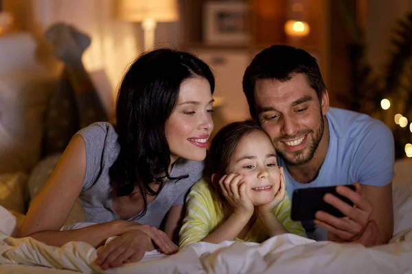 Šťastná rodina s chytrým telefonem v posteli v noci — Stock fotografie