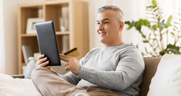 Hombre con tablet PC y tarjeta de crédito en el sofá en casa —  Fotos de Stock