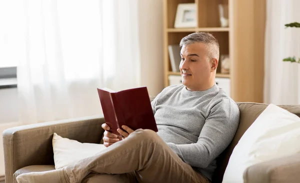 Hombre sentado en el sofá y leyendo libro en casa — Foto de Stock