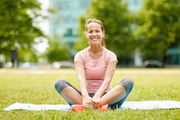 Woman sitting on exercise mat at park in summer — Stock Photo, Image