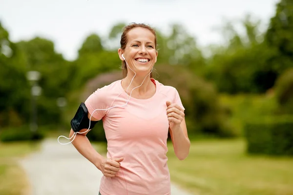 Frau mit Kopfhörer joggt im Park mit Armbinde — Stockfoto