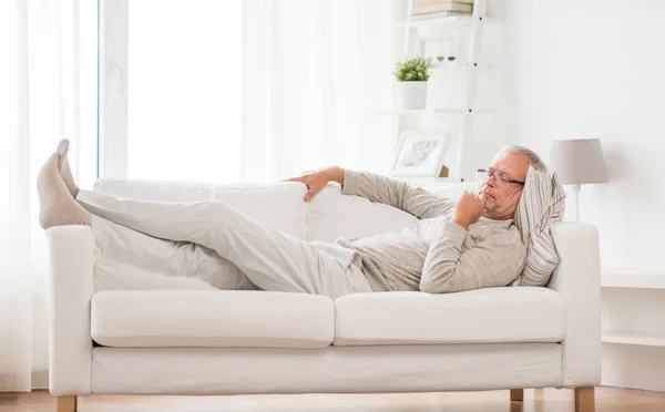 Старший мужчина лежит на диване и думает дома — стоковое фото