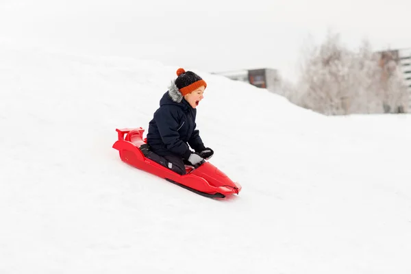 Menino feliz deslizando no trenó colina de neve no inverno — Fotografia de Stock