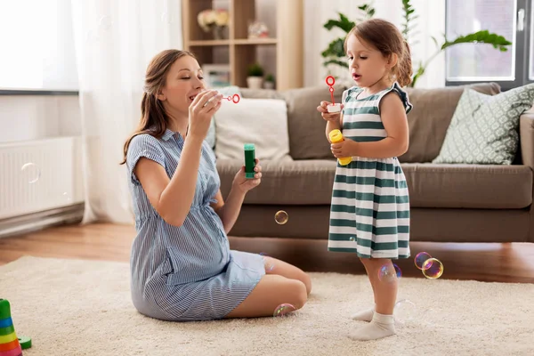 Zwangere moeder en dochter zeepbellen blazen — Stockfoto