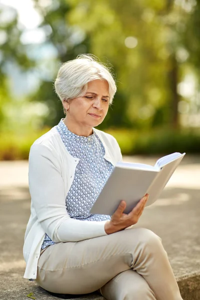 Старшая женщина читает книгу в летнем парке — стоковое фото