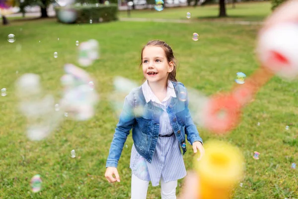 Menina feliz brincando com bolhas de sabão no parque — Fotografia de Stock