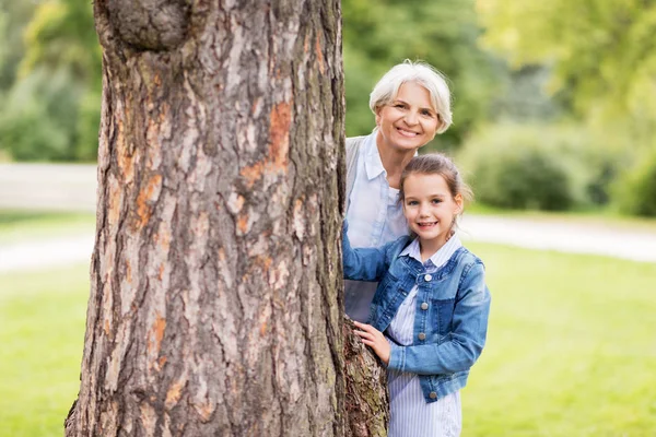 Mormor och barnbarn bakom träd på park — Stockfoto