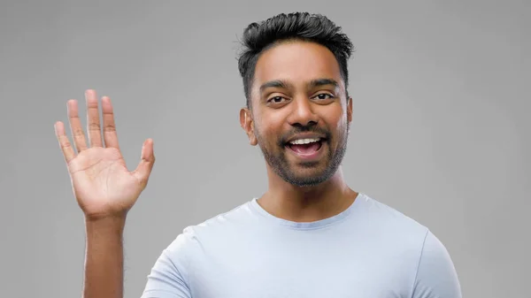 Glücklicher indischer Mann wedelt mit der Hand über grauen Hintergrund — Stockfoto