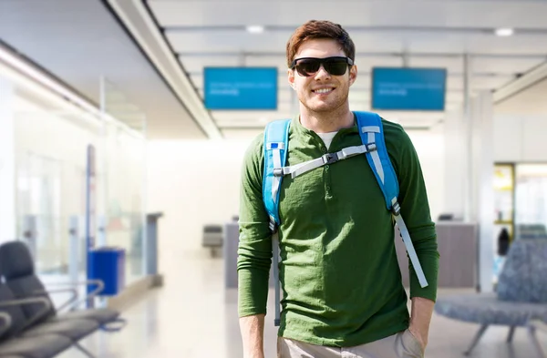 Усміхнений чоловік з рюкзаком над терміналом аеропорту — стокове фото