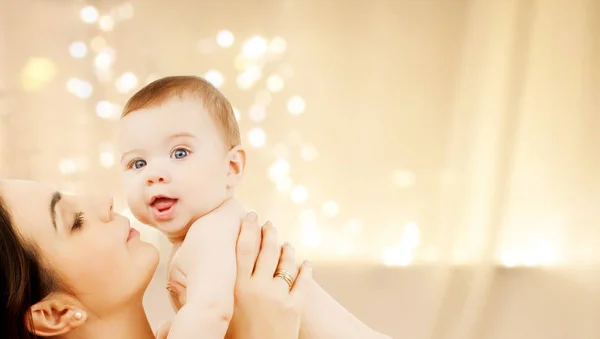 Mère embrasser bébé sur les lumières de Noël — Photo