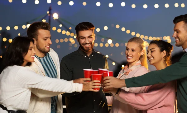 Amis cliquetis tasses de fête sur le toit la nuit — Photo