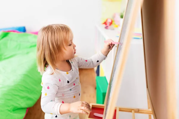 Happy little girl drawing on chalk board at home — Stock Photo, Image
