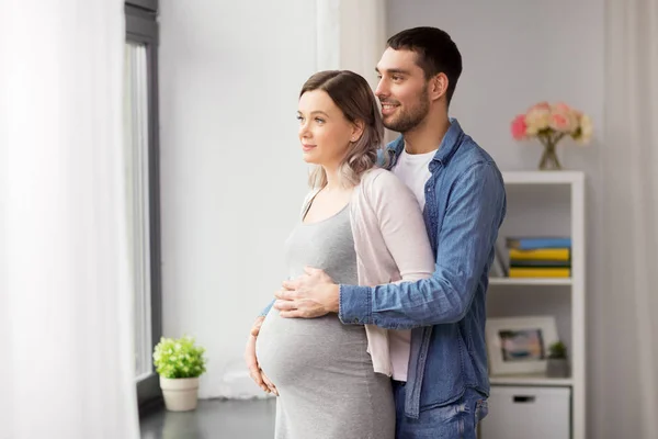 Мужчина обнимает беременную женщину у окна дома — стоковое фото