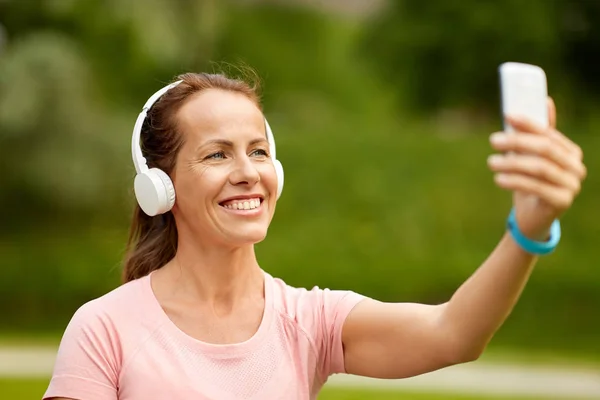 Woman in phones takes selfie by smartphone at park — Stock Photo, Image