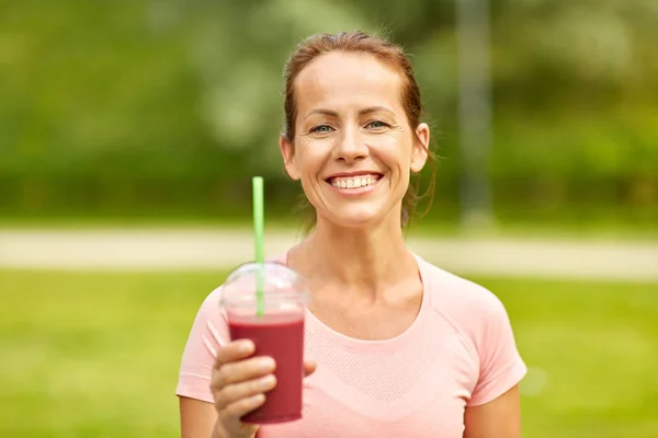 Woman drinking smoothie after exercising in park — Stock Photo, Image