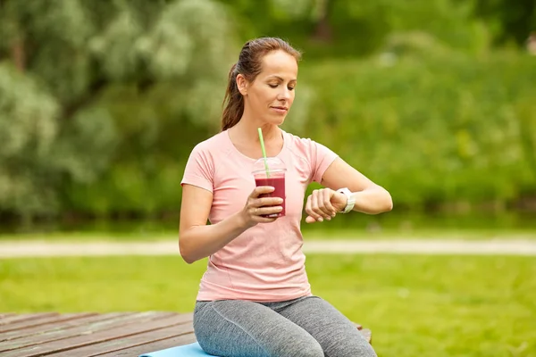 Donna con frullato guardando orologio intelligente nel parco — Foto Stock