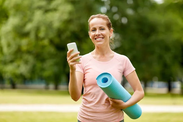 Mulher com tapete de exercício e smartphone no parque — Fotografia de Stock