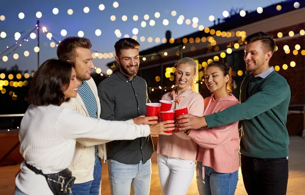 Amigos tazas de fiesta tintineo en la azotea por la noche —  Fotos de Stock