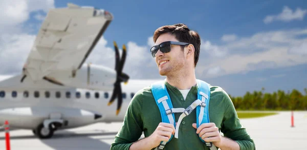 Uomo sorridente con lo zaino sopra l'aereo sul campo d'aviazione — Foto Stock