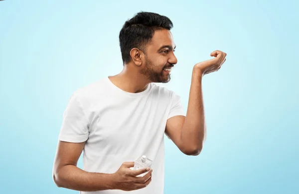 Hombre indio feliz con perfume sobre fondo azul —  Fotos de Stock