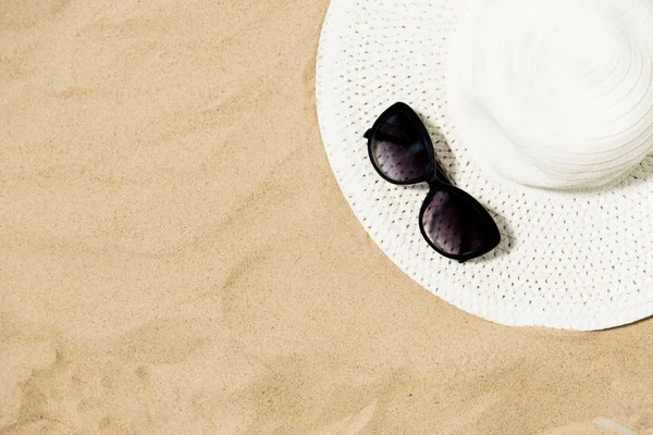 Chapéu de palha e óculos de sol na areia da praia — Fotografia de Stock