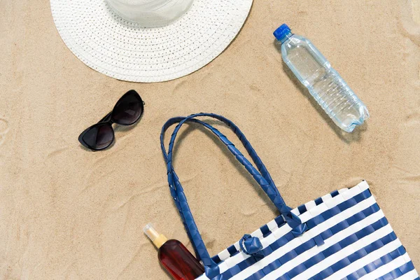 Beach bag, sunscreen, sunglasses and hat on sand — Stock Photo, Image