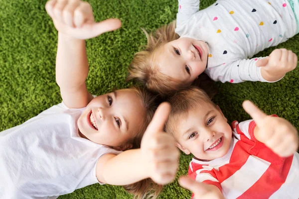 Glückliche Kinder, die auf dem Boden liegen und Daumen hoch zeigen — Stockfoto